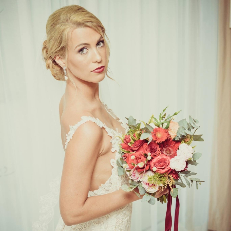 Smooch bride looks over her shoulder at the camera, showing off her makeup-while holding a bouquet.